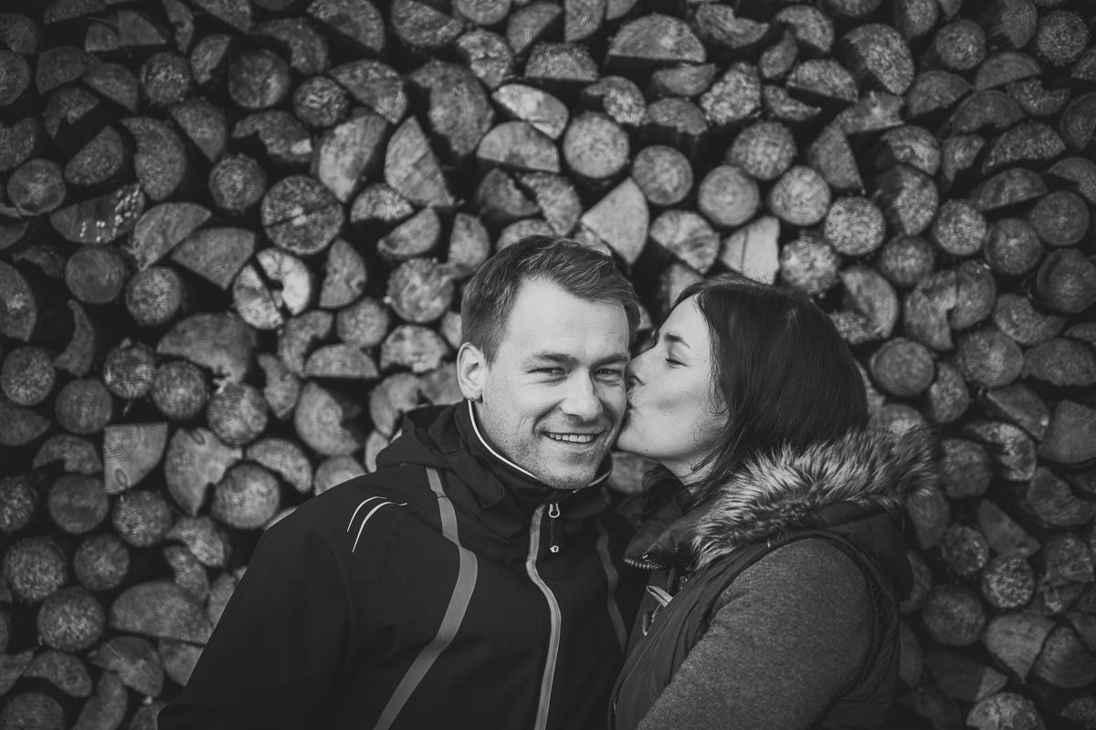 Mutter und Vater küssen sich vor einem Holzstapel